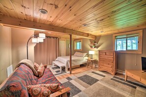 Um quarto aconchegante com uma cama, um banco, uma cômoda e uma janela com vista para árvores.