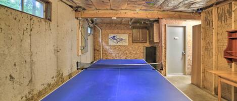 A ping pong table in a room with exposed ceiling insulation, wooden walls, and a door leading to another room.