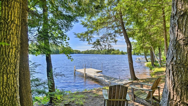 Une vue sur le lac, avec une jetée s’avançant dans l’eau, entourée d’arbres et agrémentée d’une chaise en bois.