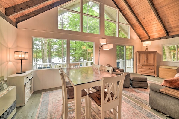 Um quarto amplo com uma grande mesa de jantar, cadeiras de madeira, um sofá e um armário. Janelas grandes permitem entrada de luz natural e oferecem vista para o exterior.