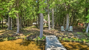 Une terrasse en bois mène à une petite maison entourée de grands arbres.