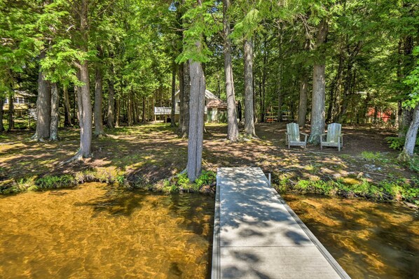 A wooden deck leading to a small house surrounded by tall trees. - Cozy Maine Lakefront Escape | Fall Foliage & Fire (Limerick)