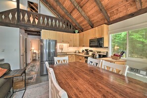 A spacious kitchen with wooden cabinets, a large dining table, and a view of the outdoors. - Cozy Maine Lakefront Escape | Fall Foliage & Fire (Limerick)