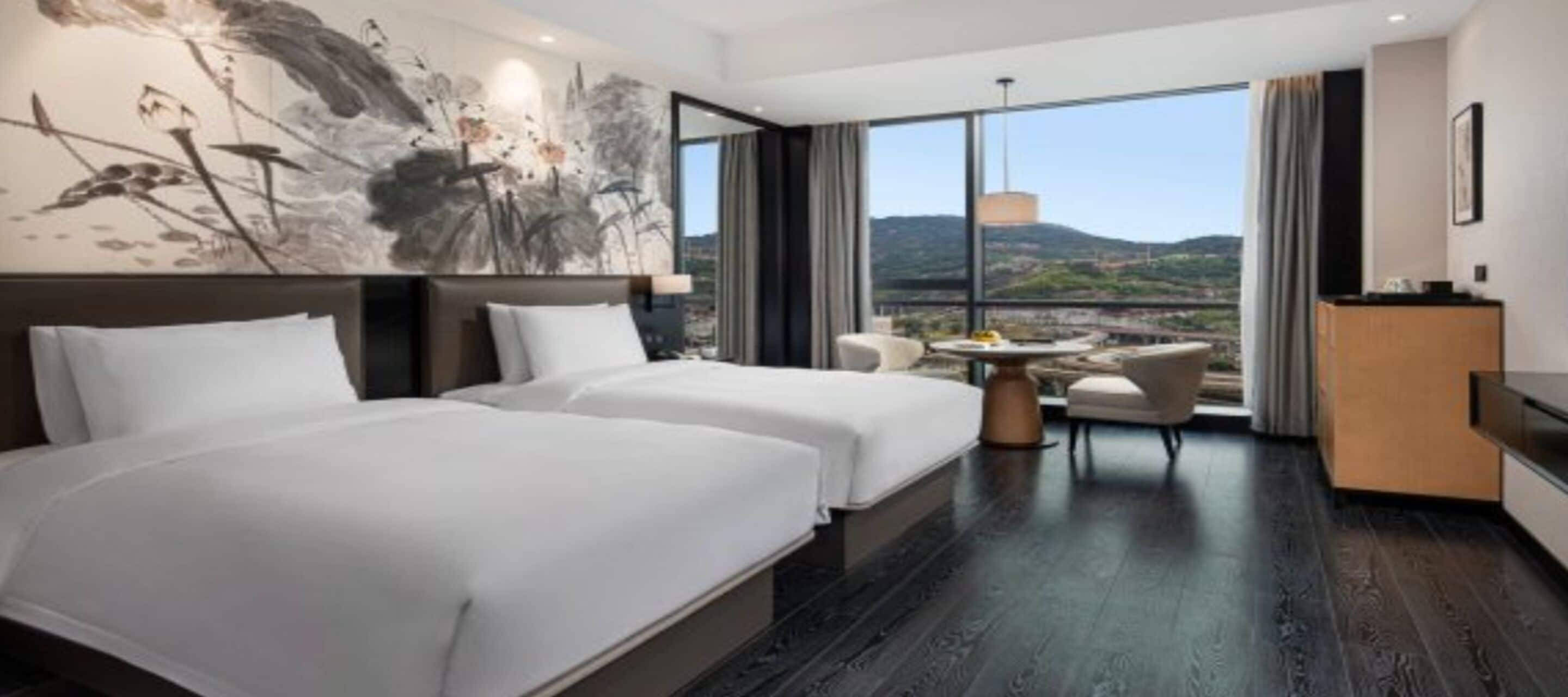 Habitación de hotel con dos camas, un rincón de comedor y un amplio ventanal con vistas al paisaje.