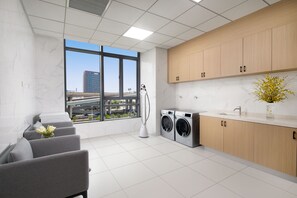 Een moderne wasruimte met een groot raam, een wasmachine, een droger en een zithoek met een bloemenvaas.