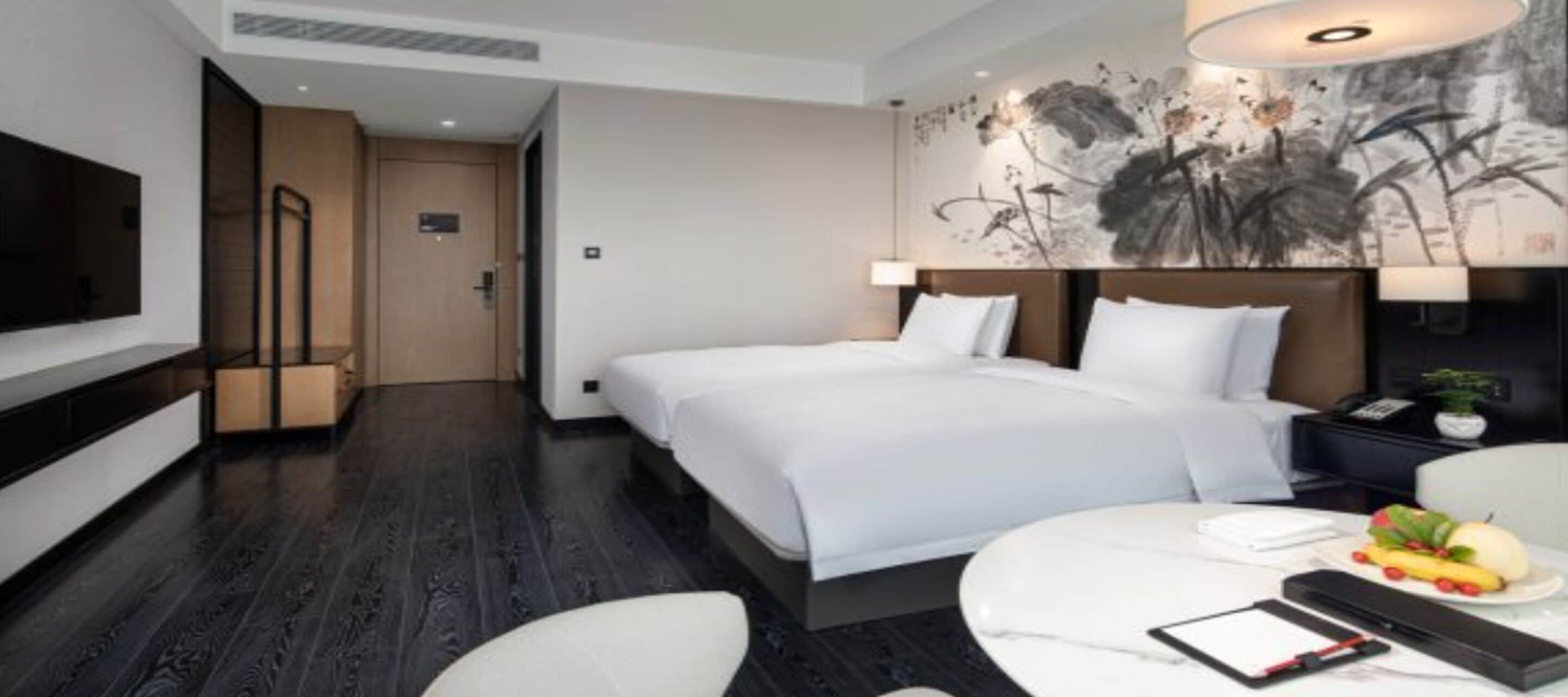 Habitación de hotel moderna con una cama grande, mesitas de noche, un televisor de pantalla plana y una obra de arte colgada en la pared.