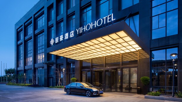 Una entrada de hotel moderna con un coche estacionado frente a ella, amplias ventanas de vidrio y un letrero que dice 