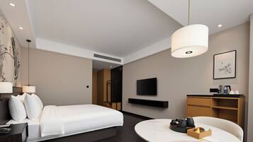 A modern hotel room with a bed, bedside table, lamp, desk, chair, and a mounted TV.