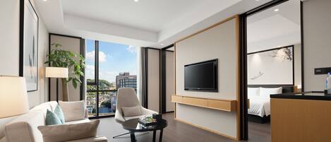 Una habitación de hotel moderna con un ventanal grande, un televisor de pantalla plana, una cama, un sofá y una mesa de centro.