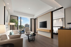 Una habitación de hotel moderna con un ventanal grande, un televisor de pantalla plana, una cama, un sofá y una mesa de centro.