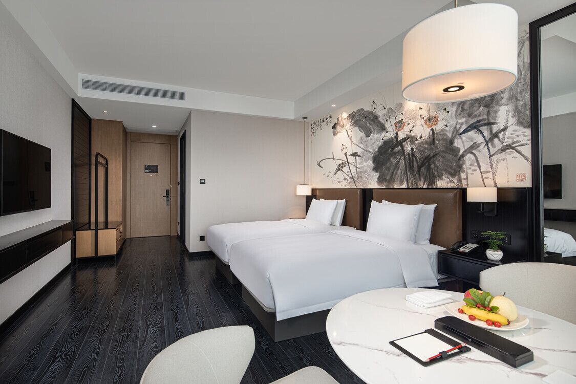 Ett modernt hotellrum med en stor säng, en platt-TV, ett matbord och ett konstverk som hänger på väggen.