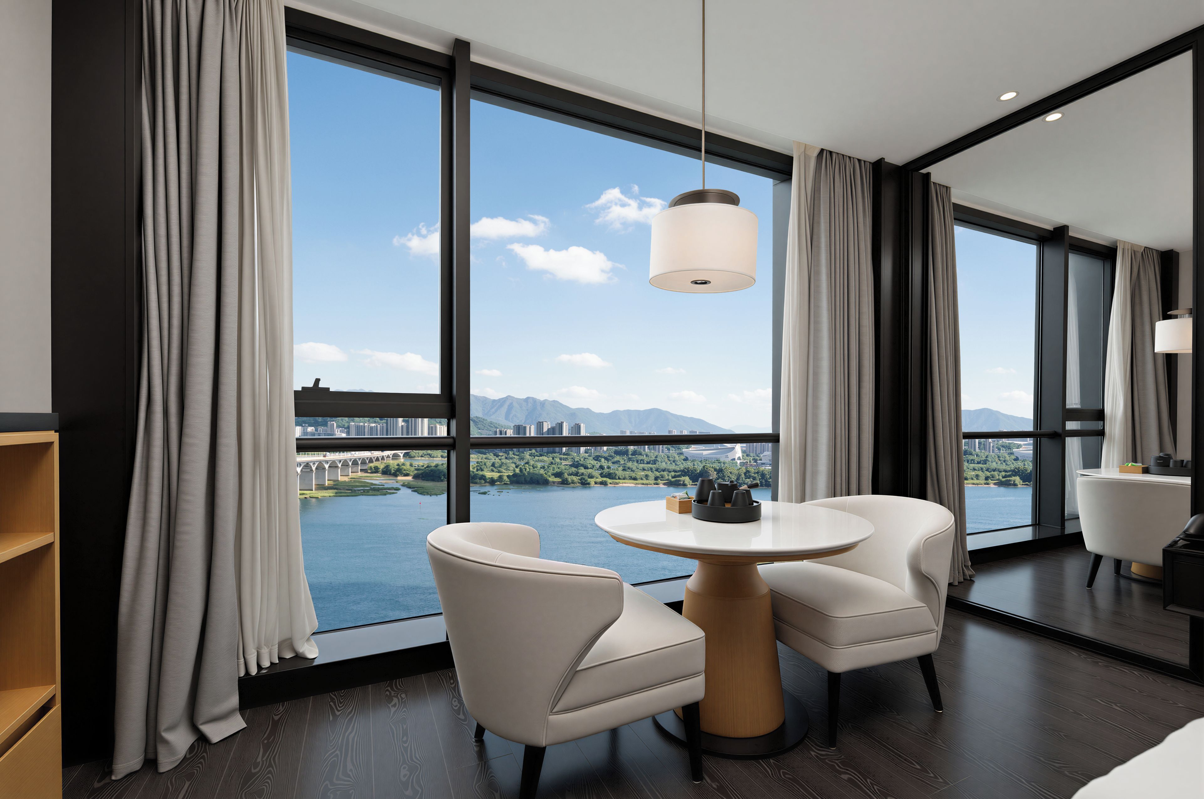 A modern hotel room with a large window, two white chairs, a round table, and a hanging light fixture.