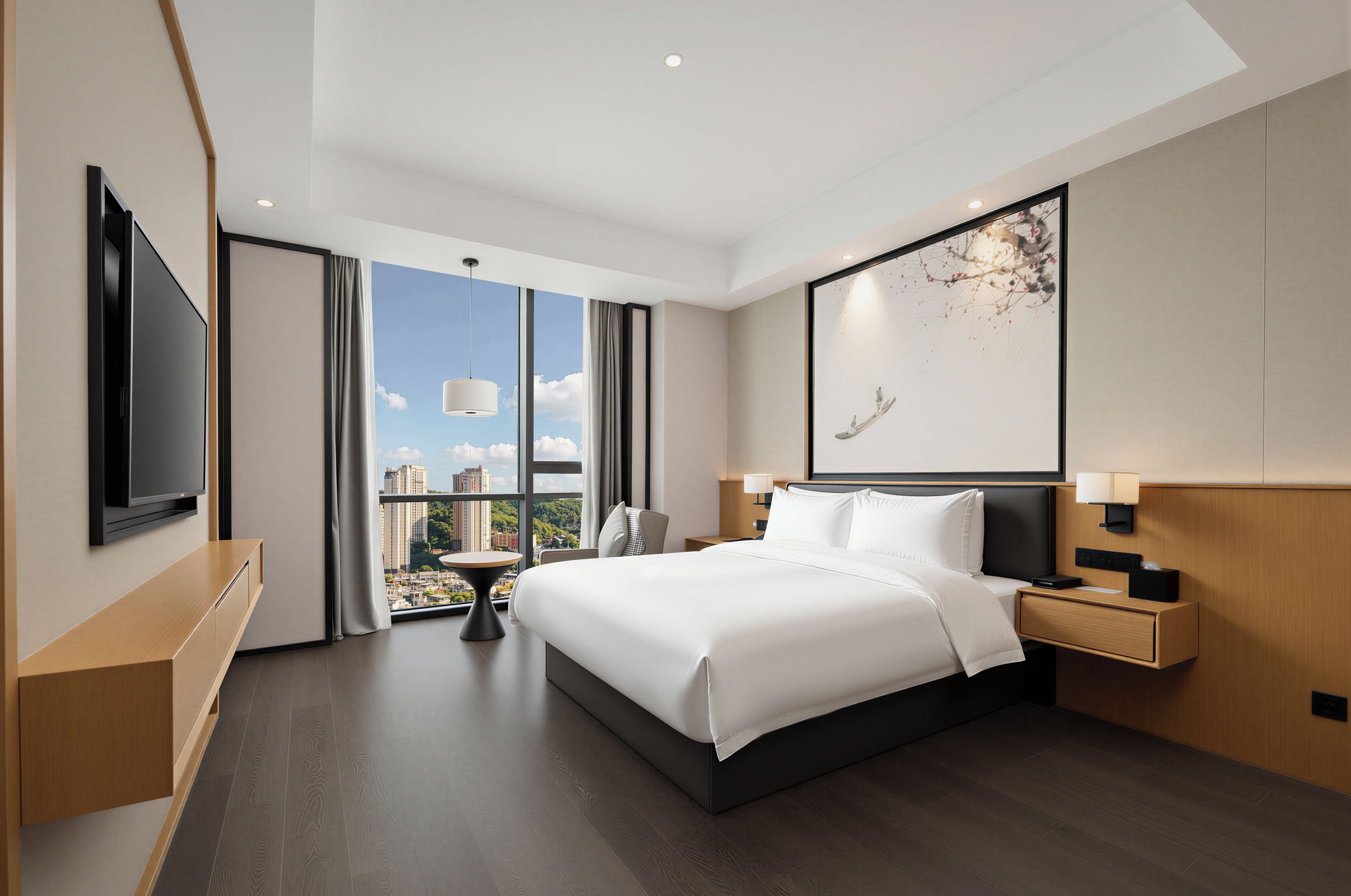 A modern hotel room with a large bed, a flat-screen TV, a desk, and a view of the cityscape.