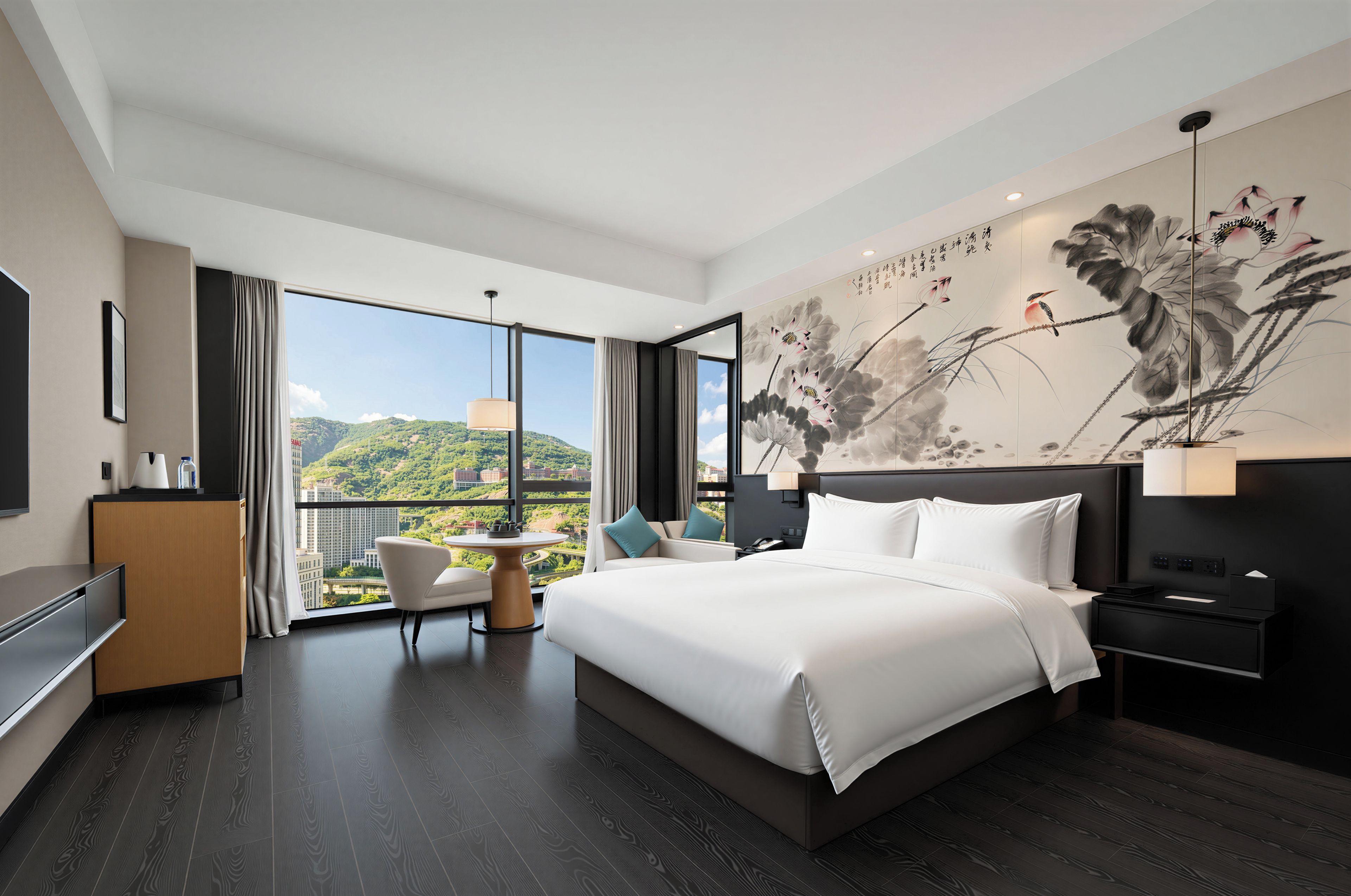 A modern hotel room with a large bed, a desk, a chair, and a view of a cityscape through the window.