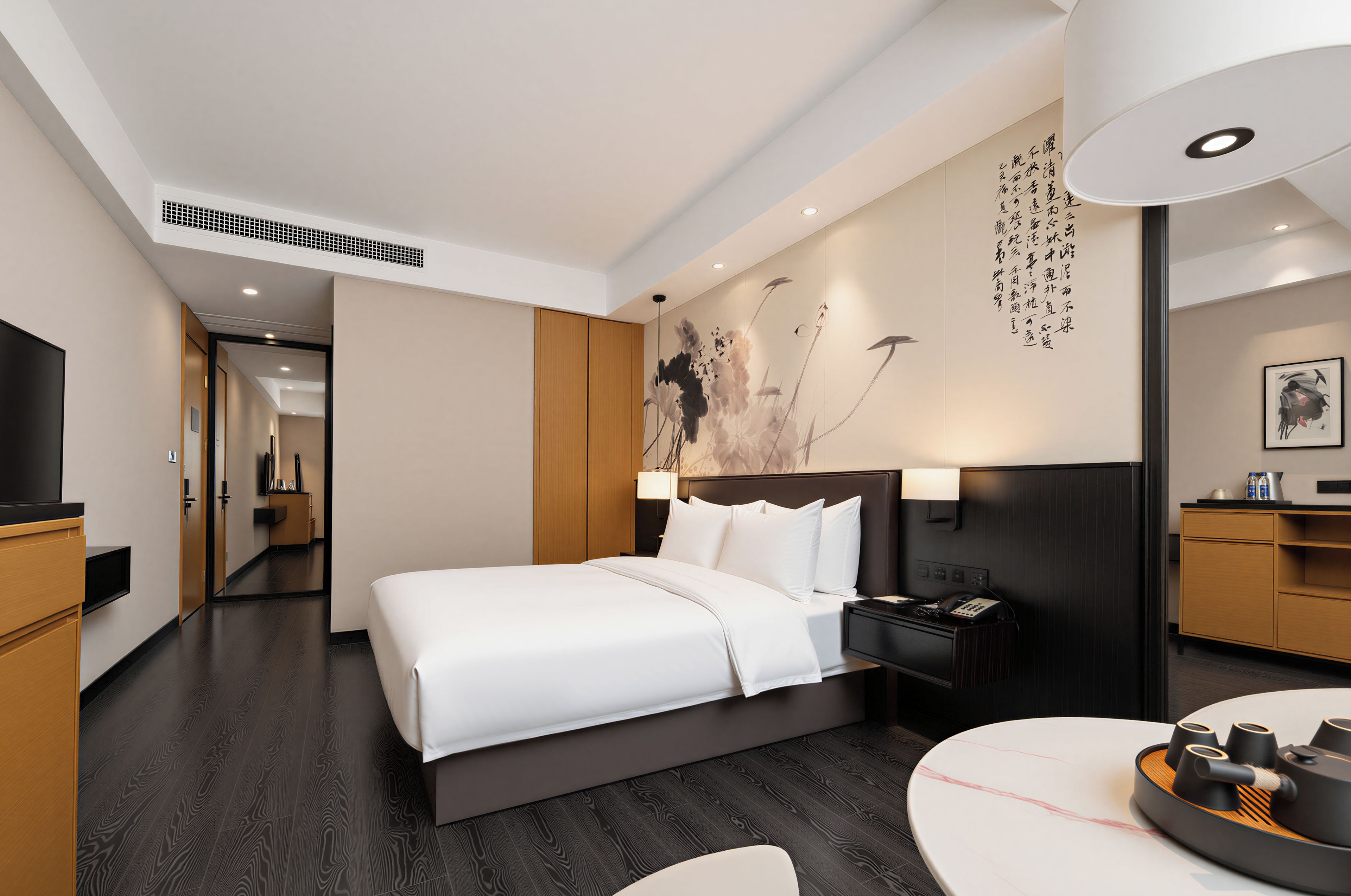 A modern hotel room with a large bed, bedside table, and a desk with a chair.