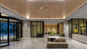 Un vestíbulo moderno con mostrador de recepción, zona de estar y puertas de vidrio que dan al exterior.