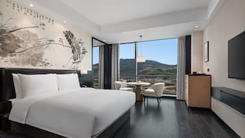A hotel room with a large bed, a desk, a chair, a TV, and a view of the outdoors.
