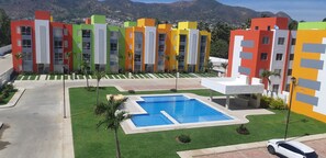 A modern residential building complex with colorful facades, a central swimming pool, and a well-maintained lawn.