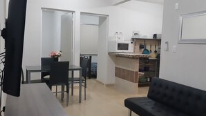 Ein kompakter Wohnbereich mit Essbereich, Küchenzeile und einem schwarzen Sofa.