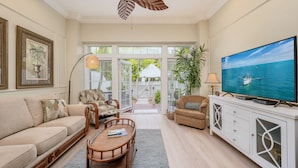 A spacious living room with a large television, comfortable seating, and a view of the outdoors through a glass door. - **CARIBBEAN CHARM** Villa Near Duval & Beach + Last Key White Glove Service... (Key West)