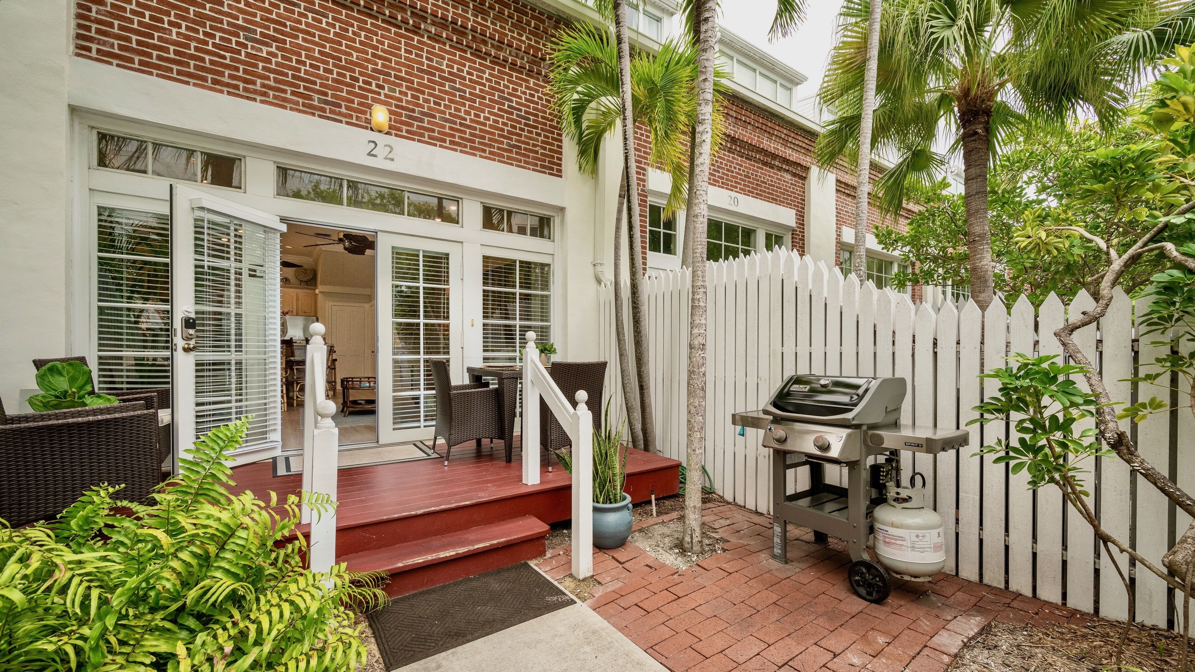 A brick building with a white fence, a grill, and outdoor seating.