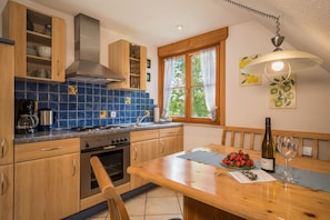 A kitchen with wooden cabinets, a stove, and a dining table with a bottle of wine and a glass.