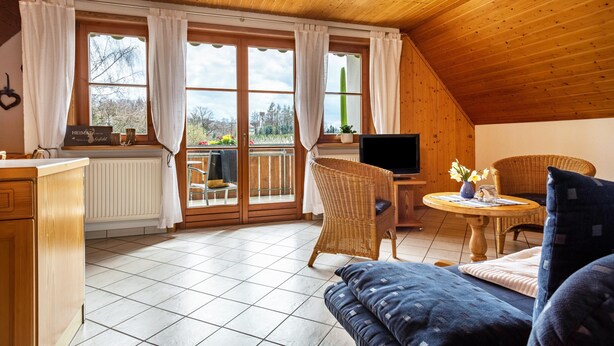 Une pièce chaleureuse avec un plafond en bois, un coin repas avec des meubles en osier, un canapé et un téléviseur.