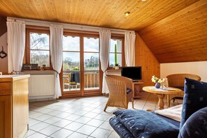 Una camera accogliente con soffitto in legno, una zona pranzo con mobili in vimini, un divano e una televisione.