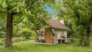 Une maison de campagne, avec une porte en bois, une cheminée en briques et un jardin où poussent différentes plantes et fleurs.