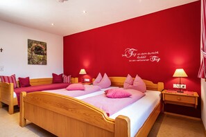 Una habitación con dos camas, una pared roja y un cuadro pequeño.