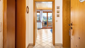 Un couloir menant à un balcon avec vue, des portes en bois et une horloge au mur.