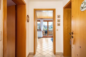 Un couloir menant à un balcon avec vue, des portes en bois et une horloge au mur.