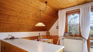 Une cuisine avec un plafond en bois, un grand îlot central, une table à manger et une fenêtre avec des rideaux.