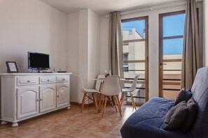 Une chambre avec un lit, un bureau avec un ordinateur, une table à manger avec des chaises et un balcon avec vue.