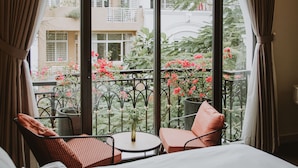 A balcony with a view of a garden and buildings. There are two chairs and a small table with a vase. - Charmaine's Hotel & Apartment (Ho Chi Minh City)