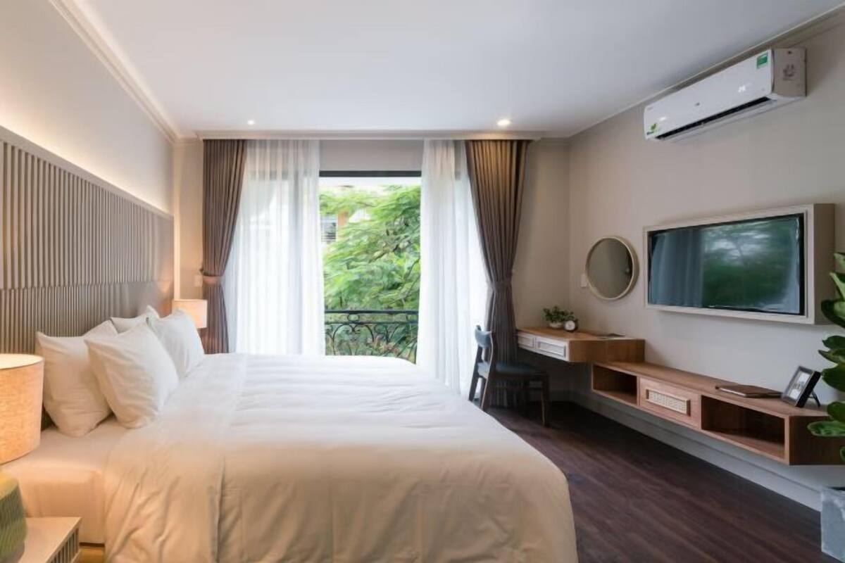 A hotel room with a bed, a desk, a TV, and a balcony with curtains.