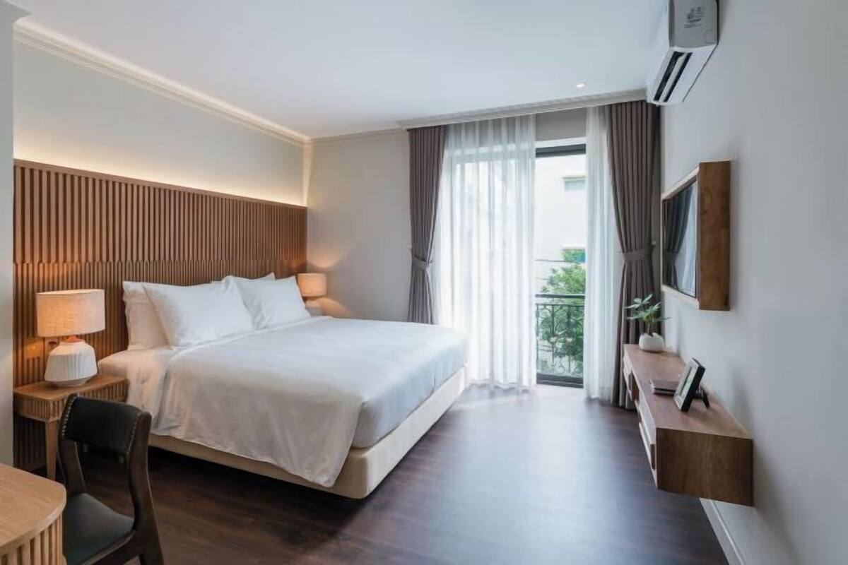 A hotel room with a large bed, bedside tables, a desk, and a view of the outdoors.