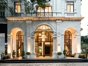 A grand hotel entrance with arched windows and a central doorway, flanked by columns and potted plants. - Charmaine's Hotel & Apartment (Ho Chi Minh City)