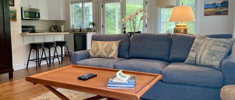A modern living room with a grey sofa, a wooden coffee table, and a kitchen in the background.