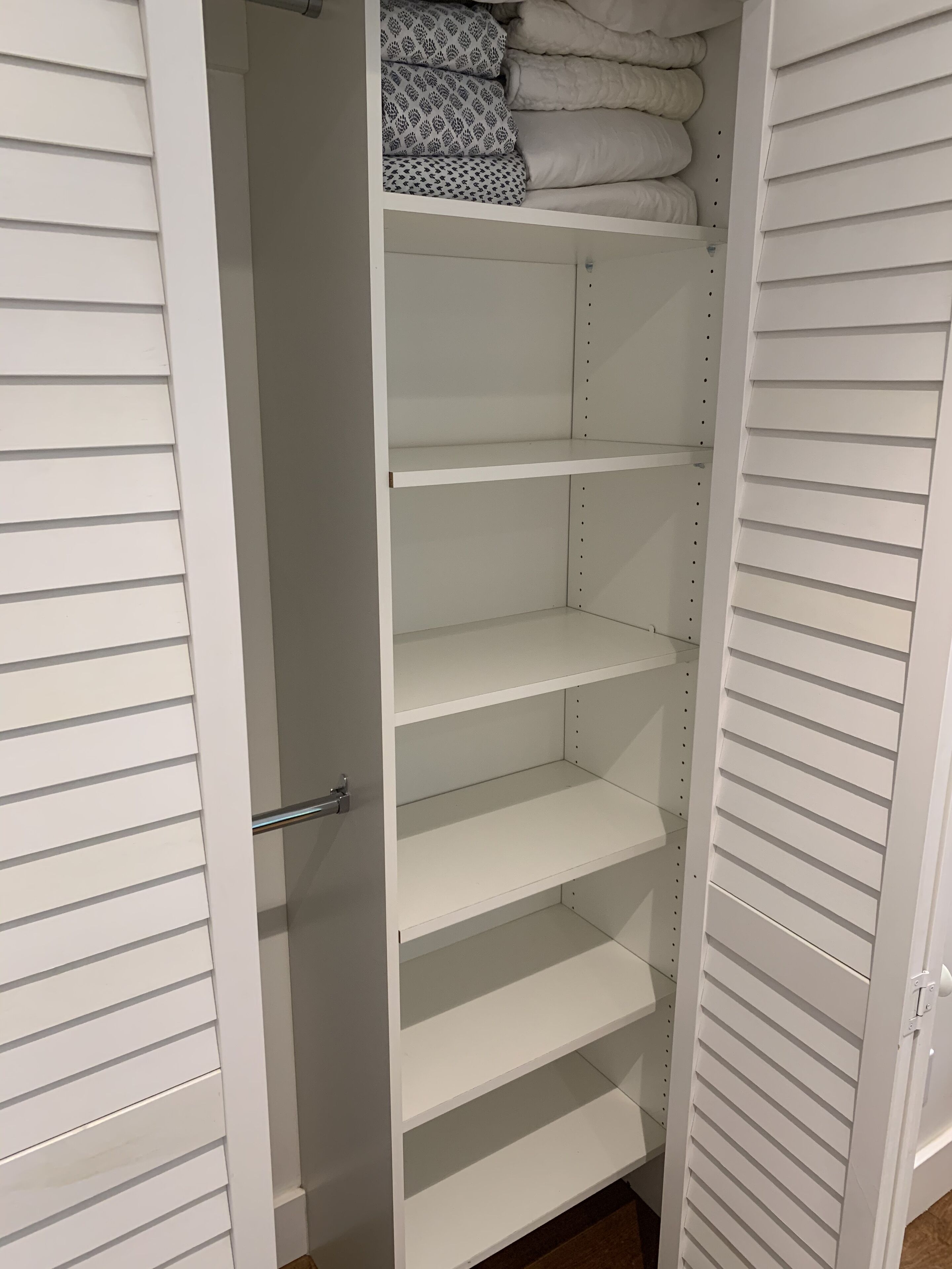 A white closet with multiple shelves and hanging space, featuring a metal handle and a small section with folded towels.