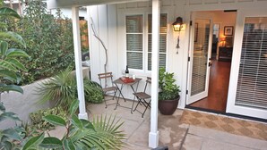 Une terrasse couverte avec une table et des chaises, un pot de fleurs et une porte portant un numéro.