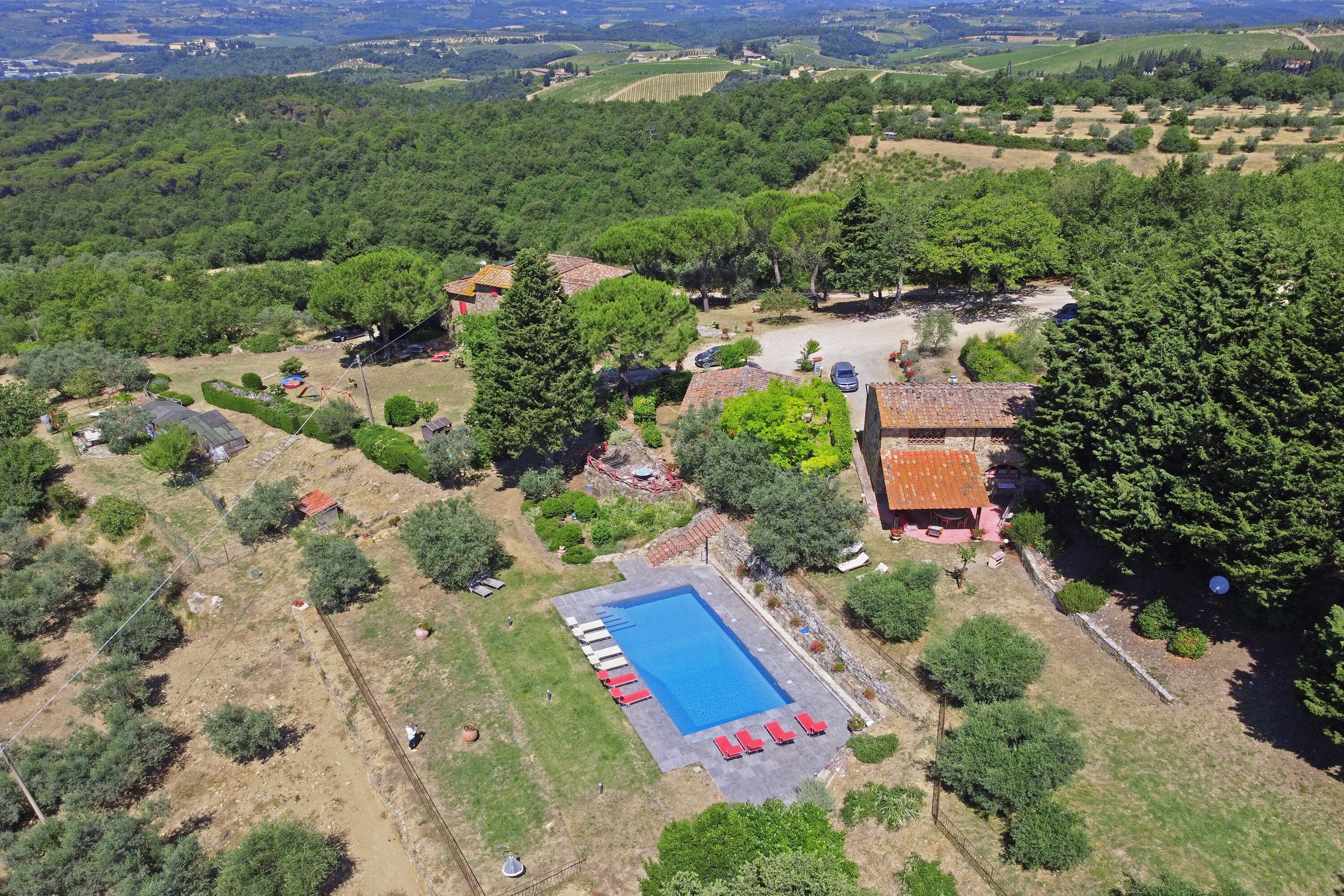 An aerial view of a property with a swimming pool, surrounded by trees and open fields.