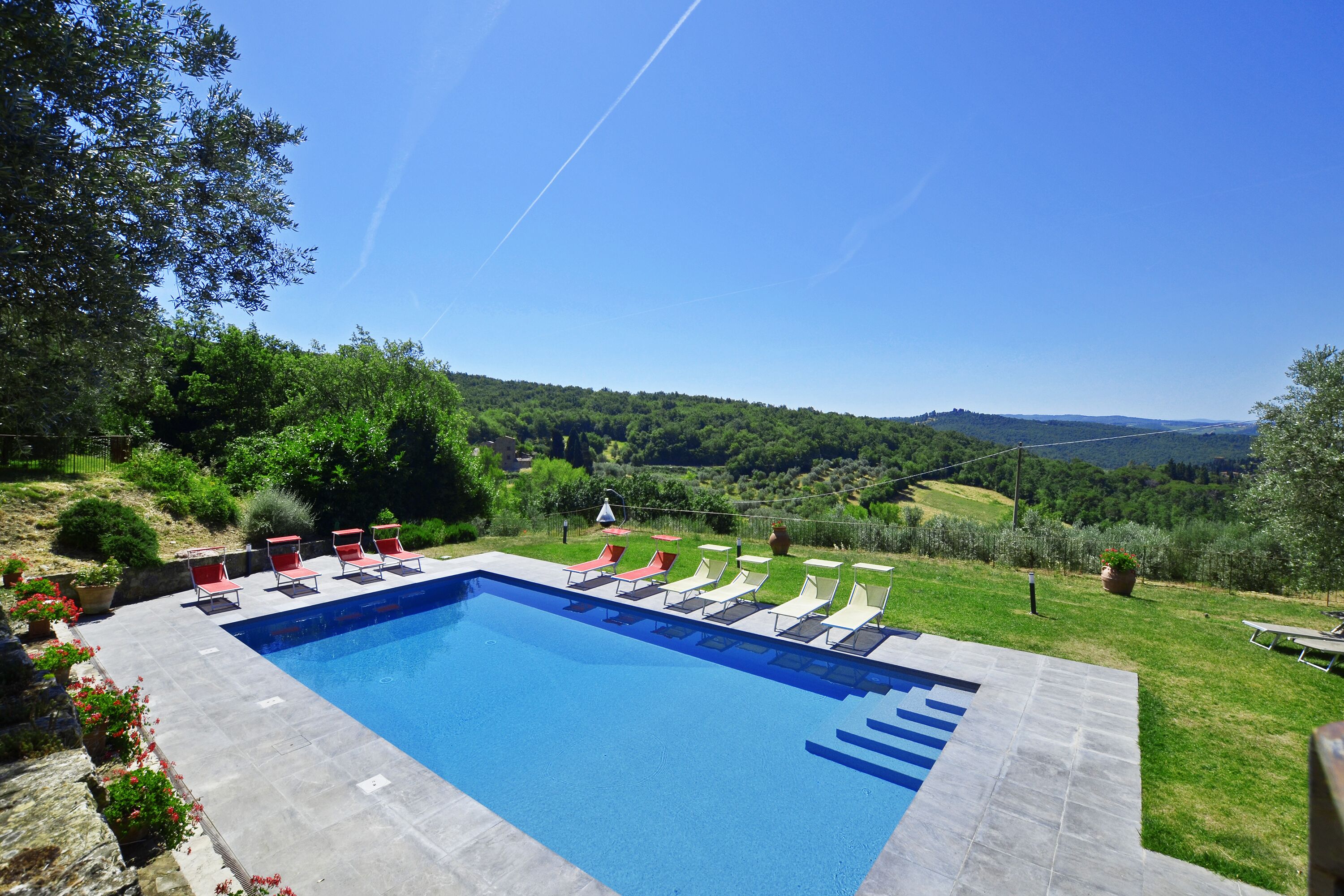 A swimming pool with lounge chairs, surrounded by a landscaped garden and a view of a hilly landscape.