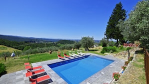 Une piscine rectangulaire à l’eau d’un bleu limpide, entourée d’une terrasse dallée où sont disposées des chaises longues rouges et blanches.