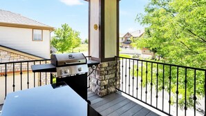 Una veranda coperta con un barbecue, un pilastro in pietra e vista su un quartiere residenziale.