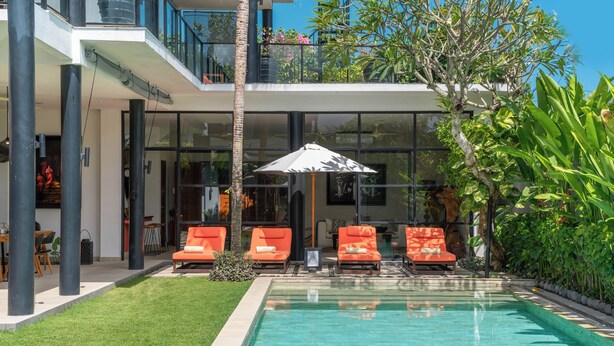 Una casa moderna con piscina, mobiliario exterior y abundante vegetación.