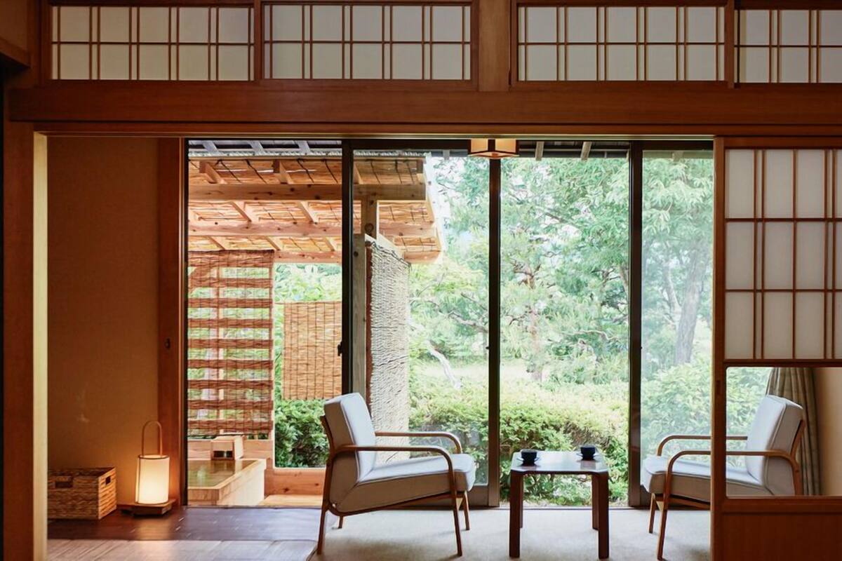 Una habitación japonesa tradicional con suelo de tatami, puertas correderas y vistas a un jardín.
