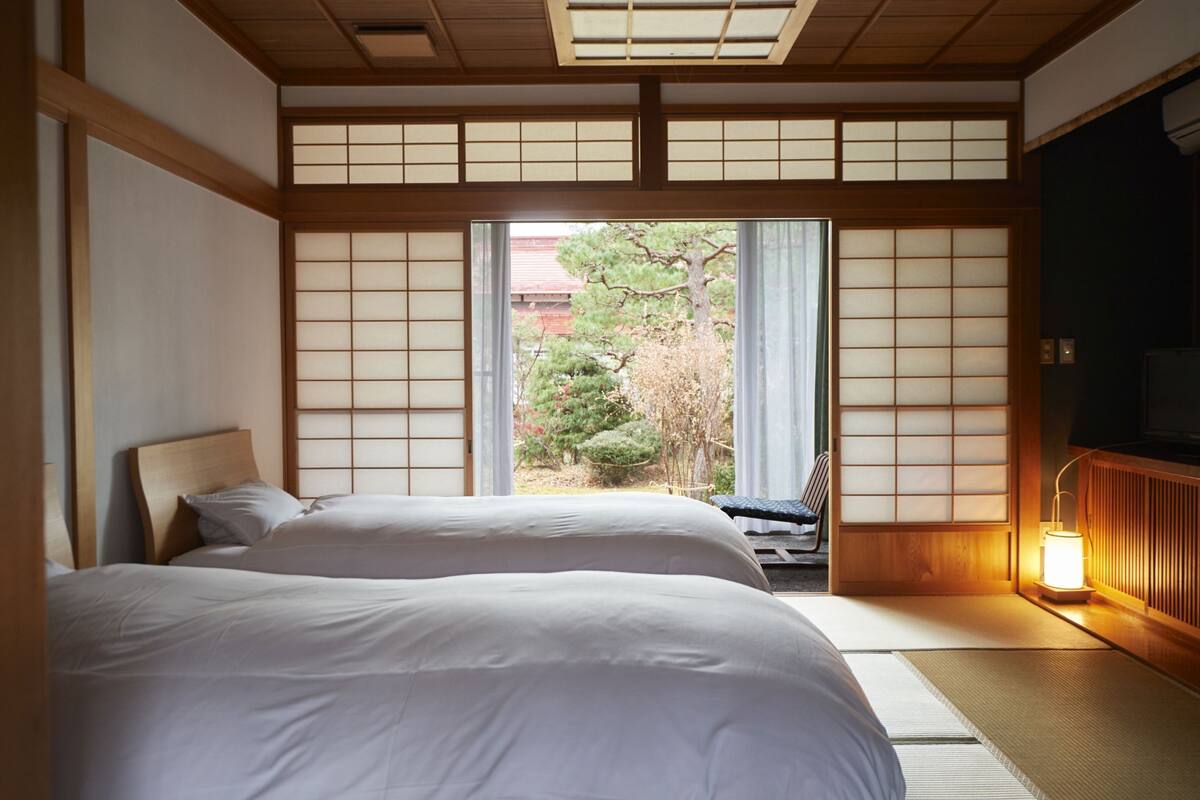 Un dormitorio tradicional japonés con suelo de tatami, una cama de madera baja y puertas correderas shoji.