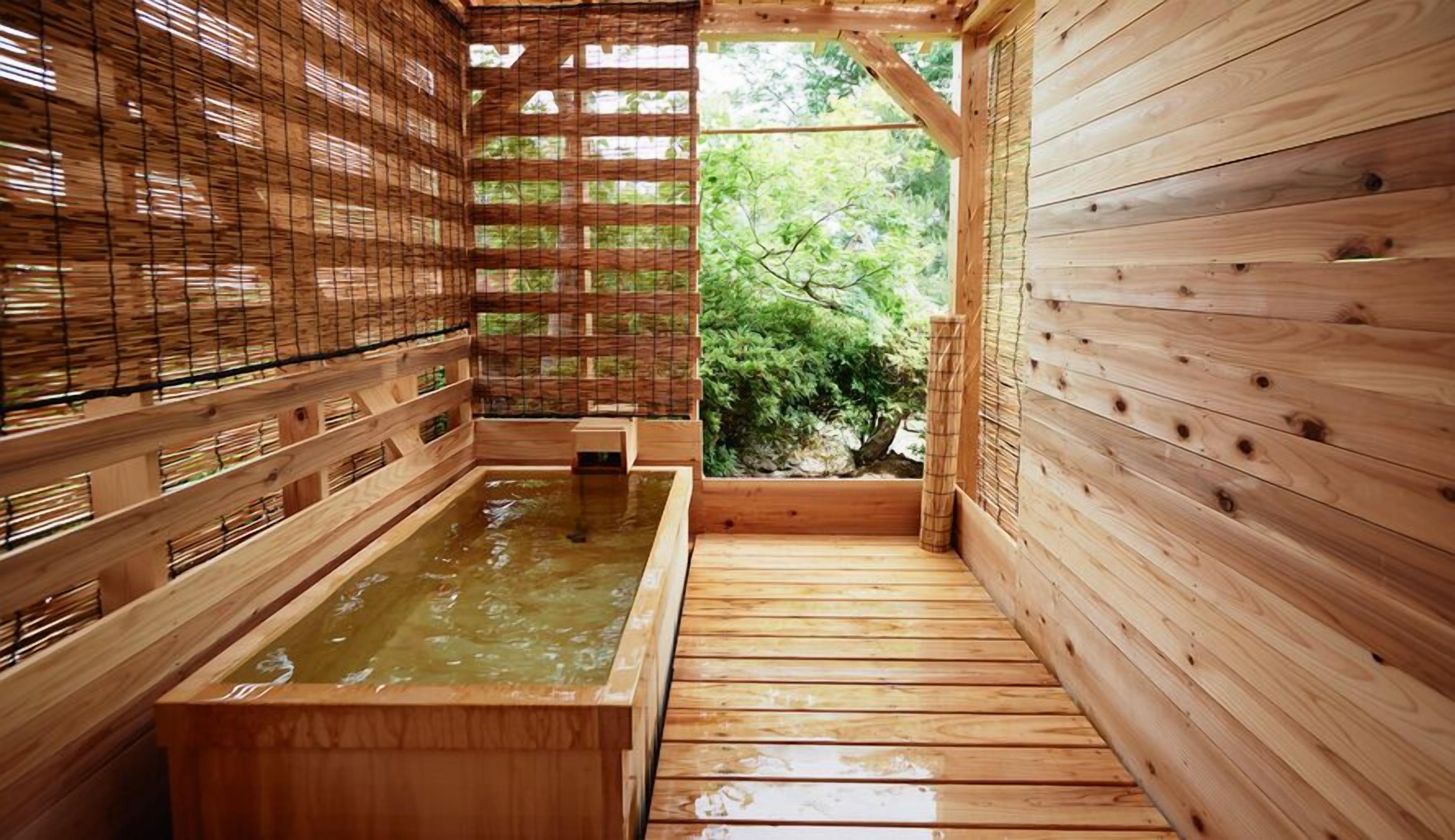 Baño de madera con aguas termales, paredes de madera y vistas a la vegetación.