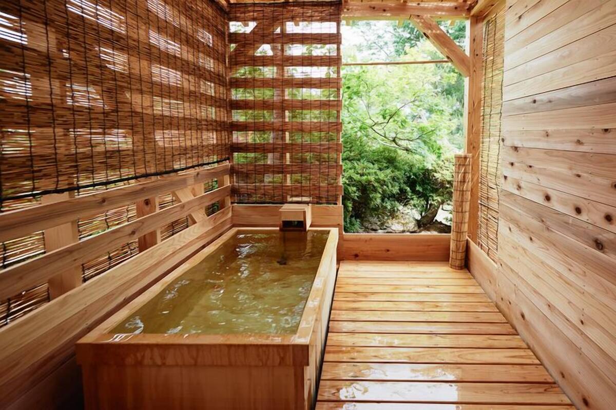 Baño de madera con aguas termales, paredes de madera y vistas a la vegetación.